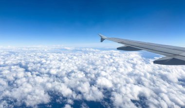 Bulutların üzerinde uçan uçak, uçak penceresinden görünen manzara, kabarık bulutlar ve mavi gökyüzü arka planı