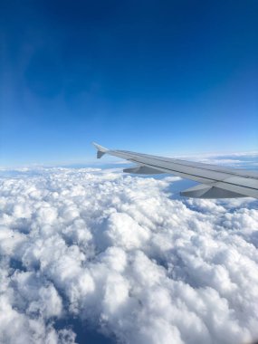 Bulutların üzerinde uçan uçak, uçak penceresinden görünen manzara, kabarık bulutlar ve mavi gökyüzü arka planı