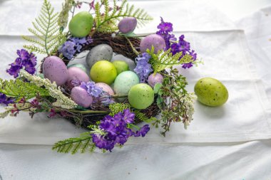 Paskalya süsü, bahar çiçekleri ve beyaz masa örtüsüne izole edilmiş Paskalya yumurtaları.