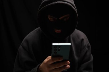 Elinde cep telefonu olan siyah başlıklı bir bilgisayar korsanı, siber suç konseptini dolandırıyor.