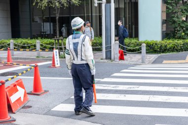 Japonya Tokyo. 13 Nisan 2024. Japon trafik kontrol sistemi. Elinde turuncu bir sopayla yaya geçidinde çalışan bir işçi.