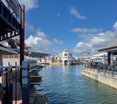 28 Ekim 2024. Güney Afrika. Knysna rıhtımında. Kafeler ve restoranlar, mavi bulutlu gökyüzü.