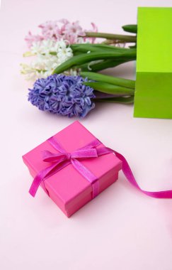 Anneler günü hediyesi. Taze sümbüller, bahar çiçekleri ve pembe arka planda bir hediye kutusu.