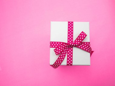 Hediye kutusu beyaz, pembe kurdele, pembe arka planda noktalar, üst manzara. Anneler ve kadınlar günü hediyesi.