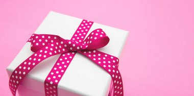 Hediye kutusu beyaz, pembe kurdele, pembe arka planda noktalar, yakın plan. Anneler ve kadınlar günü hediyesi.