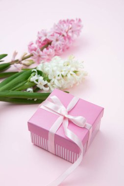 Anneler günü hediyesi. Taze sümbüller, bahar çiçekleri ve pembe arka planda bir hediye kutusu.