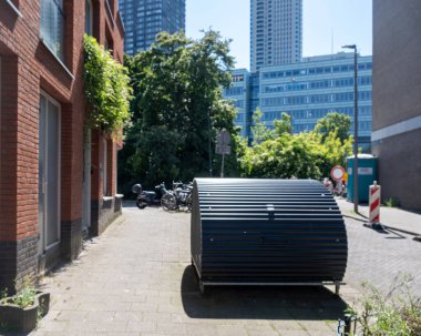 Kaldırımda üstü kapalı bisiklet parkı, arka planda bulanık binalar bisikletlerin güvenli park yeri için eğri metal yapı, Hollanda