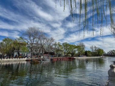 Pekin, Çin. 25 Mart 2025. Shichahai 'de göl kenarında yürüyen turistler, geleneksel Çin mimari binaları, bulutlu mavi gökyüzü..