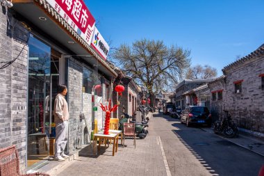 Pekin, Çin. 25 Mart 2025. Geleneksel bir Hutong caddesi. Gri tuğla binalar, kırmızı fenerler ve tanghulu sergileniyor. Açık mavi gökyüzü..