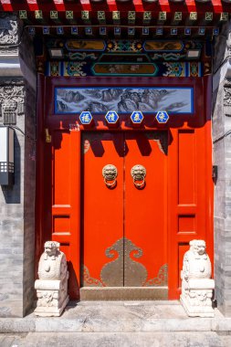Pekin, Çin. 25 Mart 2025. Geleneksel Çin kırmızı ahşap kapısı altın aslan başlıklı memeler, karmaşık oymalar ve girişte taş koruyucu aslanlar ile süslenmiş.