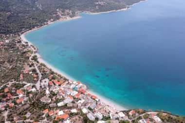 Yunanistan 'ın Porto Germeno kıyı şeridi, turkuaz sular, kumlu plaj, kıyı evleri ve yumuşak gün ışığı altında çevreleyen yeşil tepelerin insansız hava aracı görüntüsü