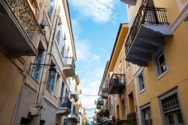 Yunanistan 'ın Nafplio kentinde dar bir sokak boyunca balkonları olan renkli neoklasik binalar. Dağınık bulutlu mavi gökyüzü