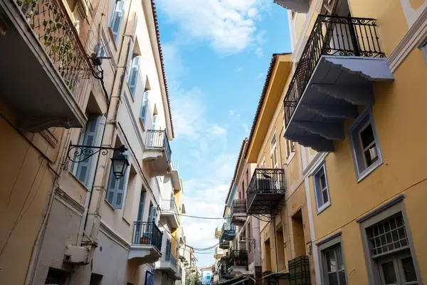 Yunanistan 'ın Nafplio kentinde dar bir sokak boyunca balkonları olan renkli neoklasik binalar. Dağınık bulutlu mavi gökyüzü