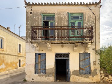 Terk edilmiş, taşralı balkonlu ve sıcak öğleden sonra güneşinin altında Yunan köyünde boyası soyulan iki katlı bir ev.