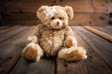 Kafasında beyaz bandajla tahta parke zeminde tek başına oturan oyuncak ayı. Çocuk yaralanması ve kaza konsepti