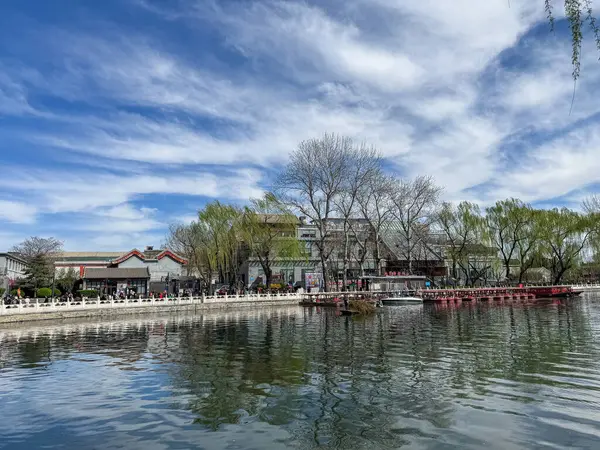 Pekin, Çin. 25 Mart 2025. Shichahai 'de göl kenarında yürüyen turistler, geleneksel Çin mimari binaları, bulutlu mavi gökyüzü..