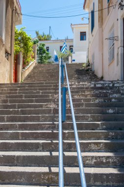 Yunanistan 'ın Poros kentindeki eski evlerin arasına uzanan geniş taştan merdivenler. Üstte Yunan bayrağı.