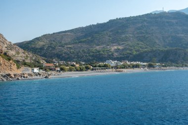 Sahil köyü Sougia ve Yunanistan 'ın güney Girit adasındaki uzun plajı. Sakin deniz ve mavi gökyüzü, engebeli tepeler