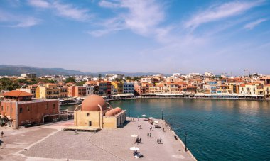 Hanya, Yunanistan, 21 Mayıs 2025. Venedik liman manzarası, Hasan Pascha camisi, renkli rıhtım binaları, durgun mavi deniz, güneşli bir gün.