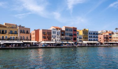 Hanya, Yunanistan, 21 Mayıs 2025. Rıhtımdaki eski Venedik liman binaları, kafelerin ve dükkanların etrafında gezinen insanlar, sakin deniz, mavi gökyüzü