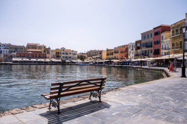 Hanya, Yunanistan, 23 Mayıs 2025. Eski Venedik liman güvertesi boyunca rıhtım binaları, dükkanlar ve kafeler ve boş bir ahşap bank.