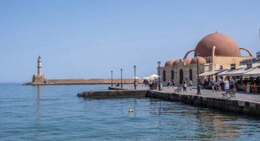 Hanya, Yunanistan, 23 Mayıs 2025. Eski Venedik limanındaki tarihi Hasan Paska Camii, rıhtım kafeleri, taş duvarlar ve Girit adasındaki deniz feneri.