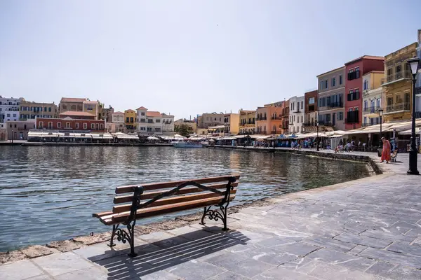 Hanya, Yunanistan, 23 Mayıs 2025. Eski Venedik liman güvertesi boyunca rıhtım binaları, dükkanlar ve kafeler ve boş bir ahşap bank.