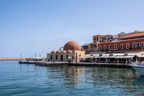 Hanya, Yunanistan, 23 Mayıs 2025. Eski Venedik limanındaki tarihi Hasan Paska Camii, rıhtım kafeleri, taş duvarlar ve Girit adasındaki renkli binalar.