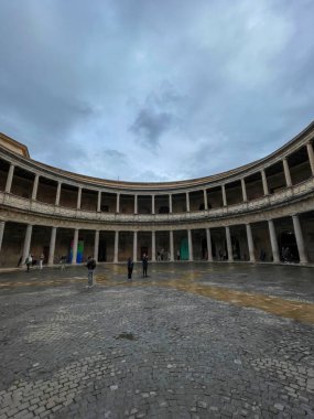 Granada, Spain, March 9, 2025. The Palace of Charles V, Renaissance architecture. Tourists on wet cobblestone, stone columns, cloudy sky