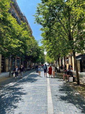 San Sebastian, Spain, May 28, 2022. The lively pedestrian street with green trees and historic buildings, people stroll and relax, sunny day