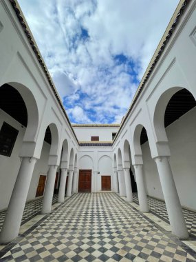 Marrakech, Morocco, March 3, 2023. Interior courtyard of Bahia Palace, islamic architecture, white arches, patterned tile floor, cloudy blue sky
