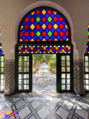 Marrakesh, Morocco, March 4, 2023.  Vibrant stained glass windows, a marble fountain and mosaic tiles at the Bahia palace courtyard