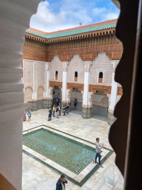 Marrakech, Morocco, March 3, 2023. Tourists at the ornate courtyard of Medersa Ben Youssef, zellij tiles and the reflective pool