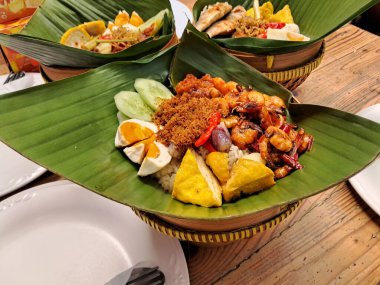 rice dishes and various side dishes packed in banana leaves on the table clipart