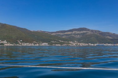 Yeşil tepeleri ve arka planında dağları olan huzurlu bir sahil kasabası, sakin mavi su, güneşli açık gün, seyahat promosyonları ve emlak tasvirleri için ideal..