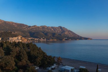 Orman tepeleri ve engebeli dağlarla çevrili güneşli kıyı kasabası, sakin mavi deniz, berrak gökyüzü, panoramik manzara, seyahat ve emlak promosyonları için ideal.