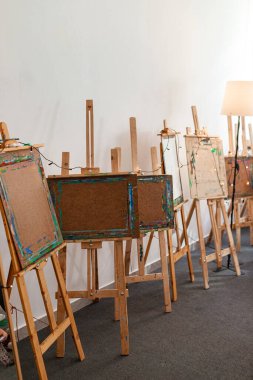 Bir sanat sınıfının içinde, üzerinde lekeli tahtalar olan birkaç boş tahta sehpa var. Sıcak iç aydınlatma sanatsal ve eğitici kullanım için uygun, gündelik, yaratıcı atmosferi vurgular.