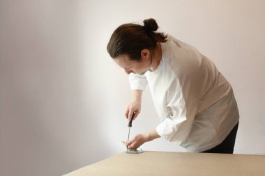 Adam dikkatle vidaları tahtaya takan yuvarlak bir metal haline getiriyor. Parlak ışıklandırma, mobilya montajında hareket ve işçiliği ön plana çıkarıyor. Beyaz gömlekli adam, içeride ahşap ve metal destek oluşturmak için tornavidayla çalışıyor..