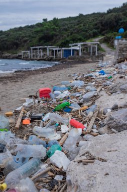 Kocaman plastik şişeler, molozlar ve okyanus kıyısına çöp yığını. Deniz çöpleri ve çevresel hasarlarla dolu bir sahil..