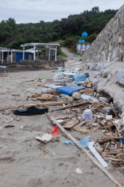 Tek siyah parmak arası terlik, kırık plastik ve okyanus yakınlarındaki kirlenmiş sahil boyunca saçılmış ahşap döküntüler. Çevre kirliliği ve kıyı kirliliği sorunu.