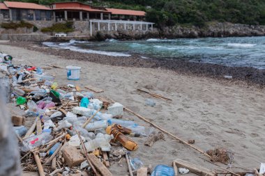 Plastik şişeler, kırık dallar ve terk edilmiş taş binaların yakınındaki kumlu sahil boyunca yığılmış deniz enkazı. Çevre kirliliği ve okyanus kirliliği sorunu.