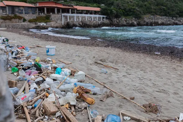 Plastik şişeler, kırık dallar ve terk edilmiş taş binaların yakınındaki kumlu sahil boyunca yığılmış deniz enkazı. Çevre kirliliği ve okyanus kirliliği sorunu.