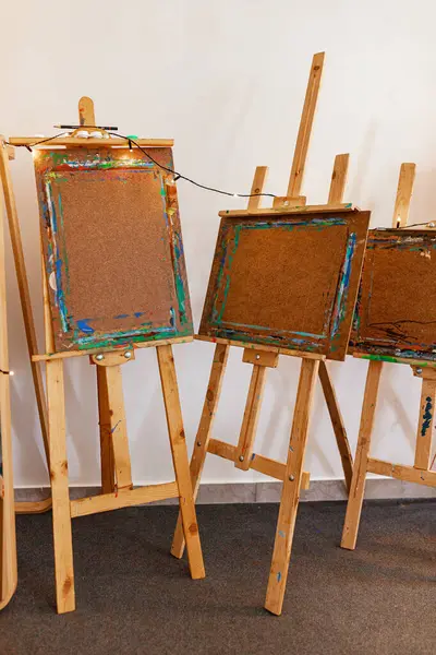 Yayın ışıklarıyla çerçevelenmiş, ağır kullanımla sanat sehpalarının yatay görünümü. Bir panelde iç mekan çizimi var. Yaratıcı ya da sanat temalı editör içeriği için mükemmel.