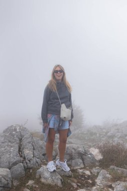 Çift, sonbahar yollarında dağdaki sislere bakıyor. Kol kola duran çift, sisli orman patikalarına, altın yapraklara, sise ve kayalık kenarlara bakıyor. Açık havada sakin bir atmosfer yaratıyor..