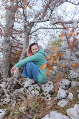 Çift, sonbahar yollarında dağdaki sislere bakıyor. Kol kola duran çift, sisli orman patikalarına, altın yapraklara, sise ve kayalık kenarlara bakıyor. Açık havada sakin bir atmosfer yaratıyor..