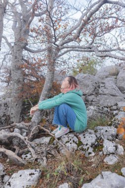Çift, sonbahar yollarında dağdaki sislere bakıyor. Kol kola duran çift, sisli orman patikalarına, altın yapraklara, sise ve kayalık kenarlara bakıyor. Açık havada sakin bir atmosfer yaratıyor..
