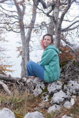 Çift, sonbahar yollarında dağdaki sislere bakıyor. Kol kola duran çift, sisli orman patikalarına, altın yapraklara, sise ve kayalık kenarlara bakıyor. Açık havada sakin bir atmosfer yaratıyor..