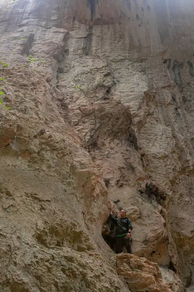İnsan keskin katmanlı, dikey mağara duvarına dayanır. Dev dikey taş duvarın yanında duran erkek yürüyüşçü, dramatik doğal desenler, ince bitki örtüsü, mağara gölgeleri güçlü derinlik ve ölçek duygusu yaratır.