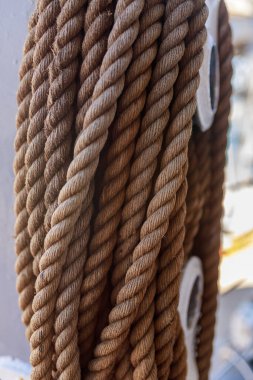 Metal makara elementine sarılı bükülmüş kahverengi gemi ipleri. Doğal iplik ve sarmal üzerine keskin bir odaklanmayla yelken halat dokusunun Macro detayı. Yelkenli tekneye sabitlenmiş donanım, yumuşak arkaplanla çerçevelenmiş..