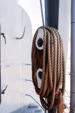 Çelik duvara karşı çift makara ile sarmalanmış kalın kahverengi denizcilik halatı. Metal kirişlerin yanına monte edilmiş, çift beyaz makara üzerinde engebeli halat halkaları. Yumuşak gölgeli deniz manzarası, sarmal deseni açıkça belirtilmiş..